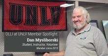 OLLI at UNLV Member Spotlight Dan Mysliborski standing smiling in front of UNLV banner in glass case